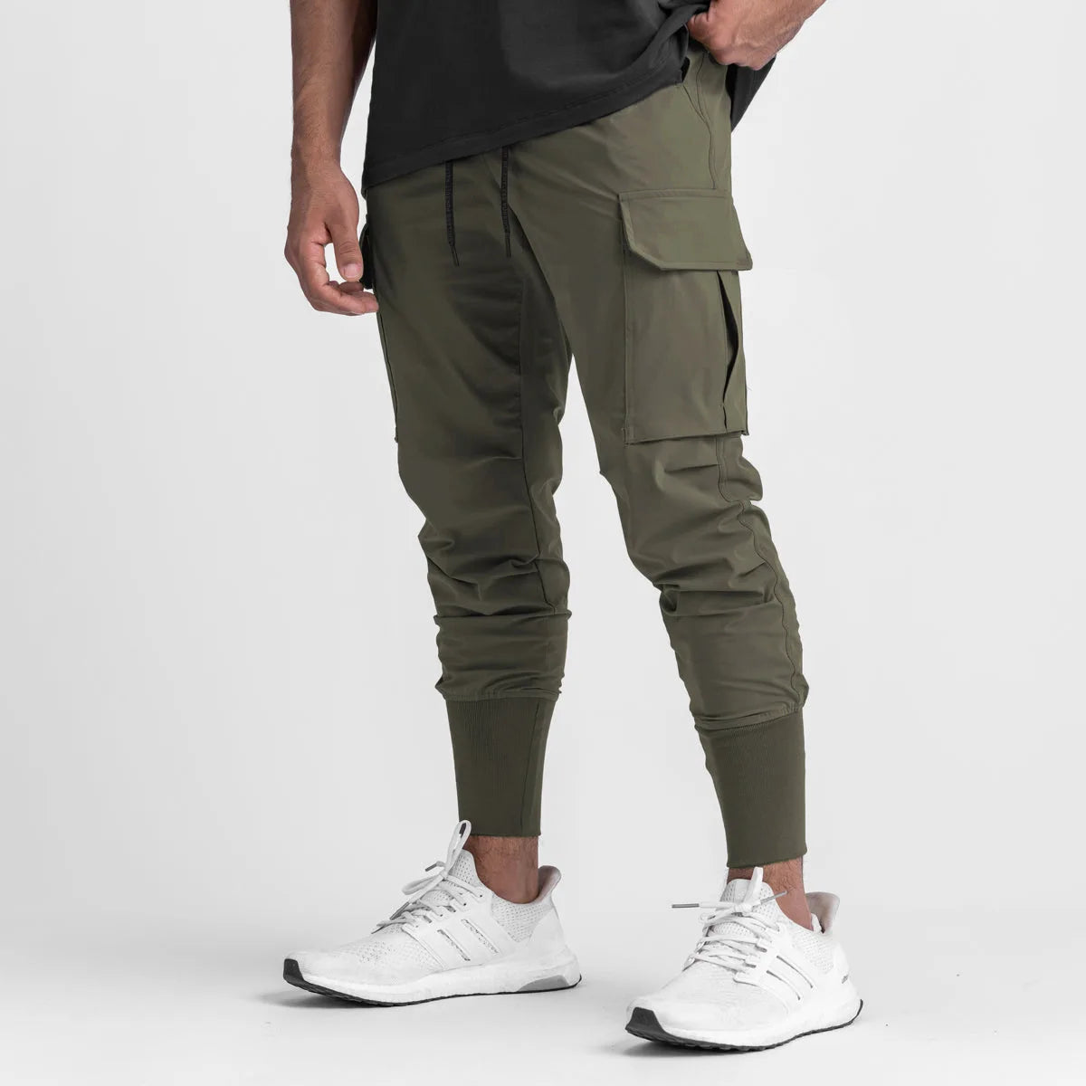 Men's cargo style sports pants in olive green, featuring a drawstring closure and cuffs, paired with athletic shoes.