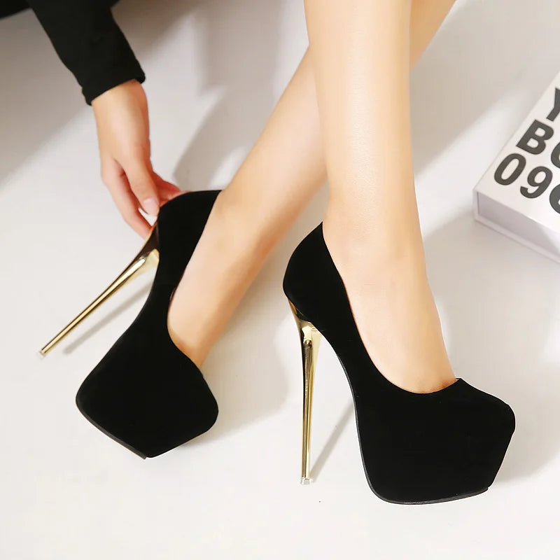 Black high-heeled shoes with gold tips worn by a person on a white background