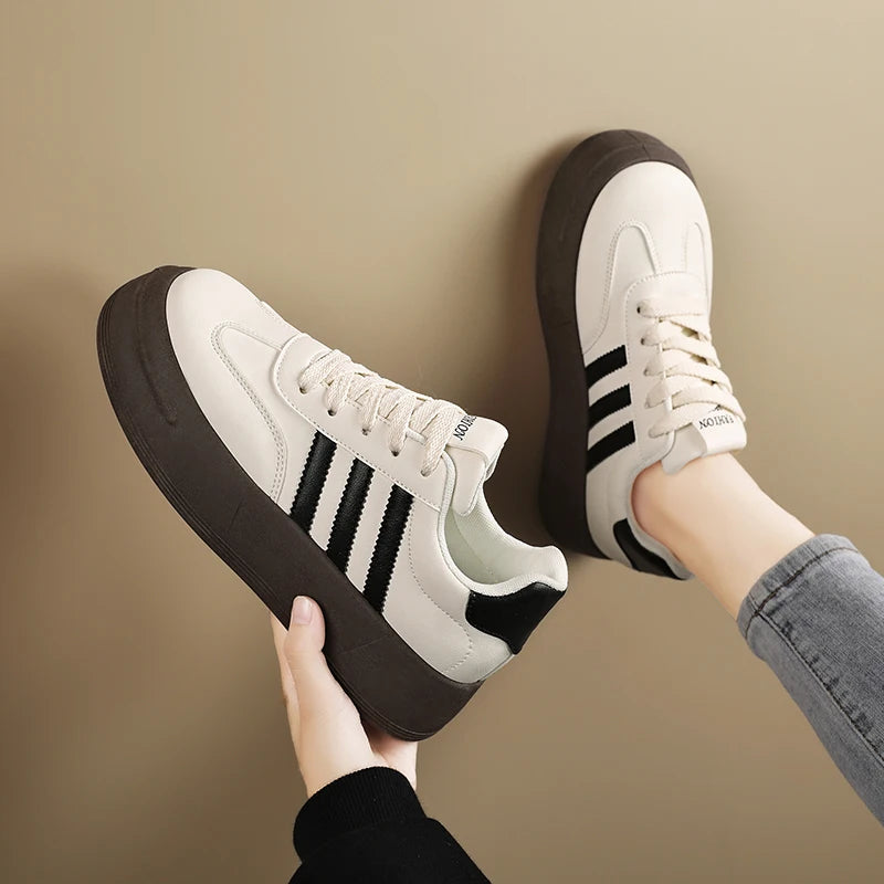 White sneakers with black stripes held by a person against a beige background