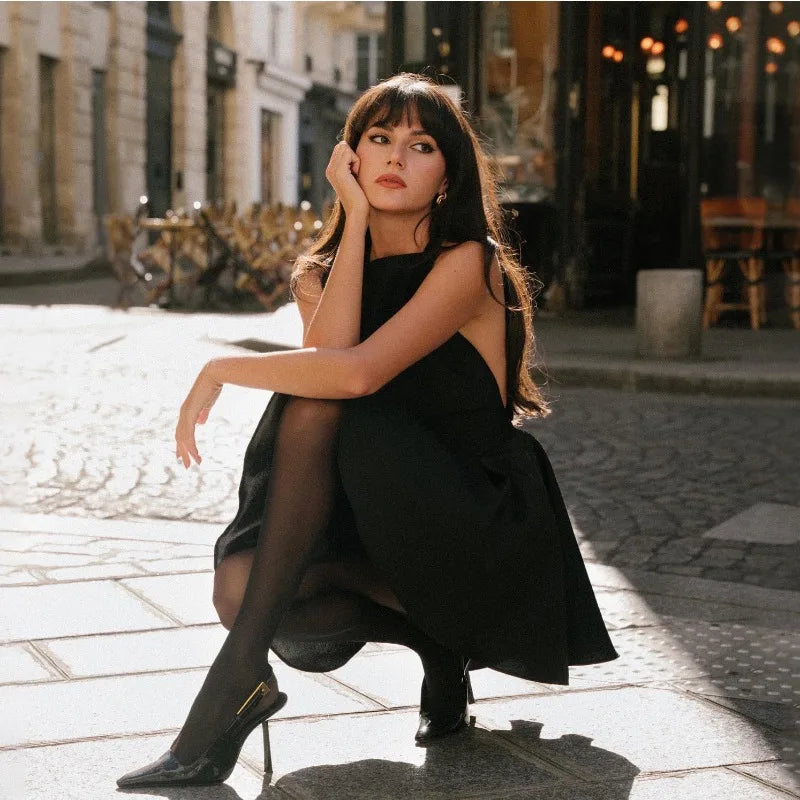 Woman in a chic black halter dress sitting on urban street, showcasing elegance and style.