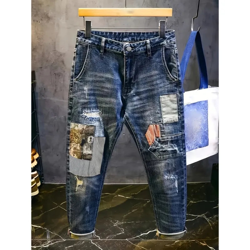 Distressed blue jeans with patchwork design on a hanger against a gray wall.