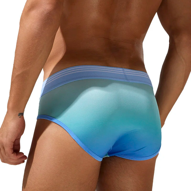 A close-up back view of a male model wearing a pair of men's briefs with a blue and teal gradient design and a light blue striped waistband, set against a solid white background.