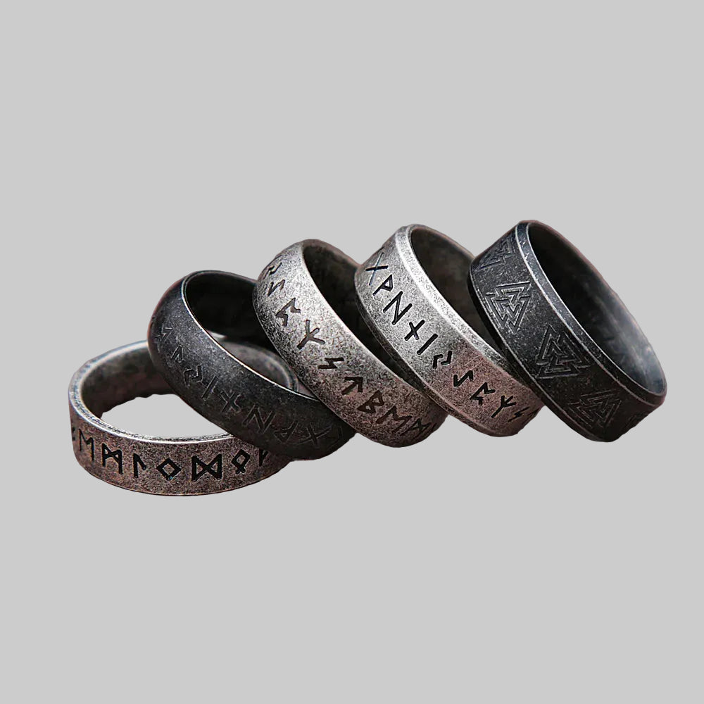 Set of five metallic rings with engraved designs on a wooden surface