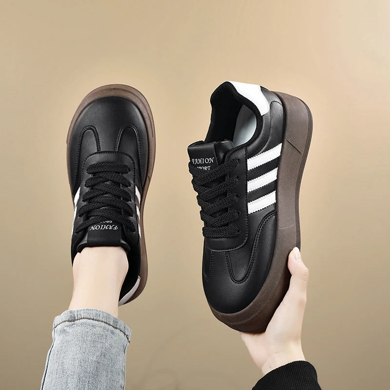 Black and brown sneakers with white stripes held by a hand against a beige background