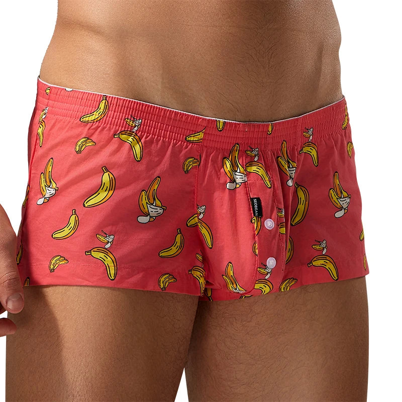 Men's boxer briefs in a coral red color, featuring an all-over print of yellow bananas and cartoon characters, shown on a model.