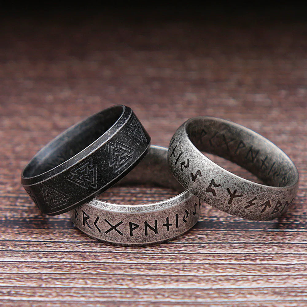 Three metallic rings with engraved designs on a wooden surface