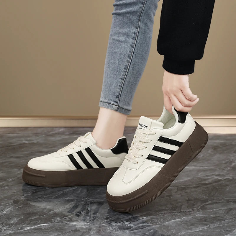 White sneakers with black stripes worn by a person on a marble floor.
