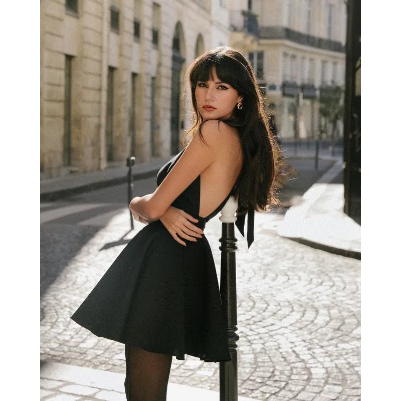Stylish model wearing a black halter dress standing on a cobblestone street, showcasing an elegant design and a chic silhouette.