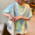 Model wearing a pastel tie-dye t-shirt with a casual fit, holding a tote bag in a cozy indoor setting.