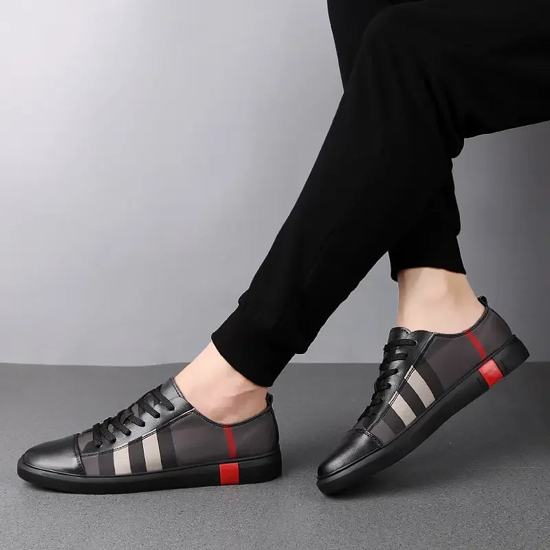 Black leather shoes with red and gray stripes worn by a person on a gray background