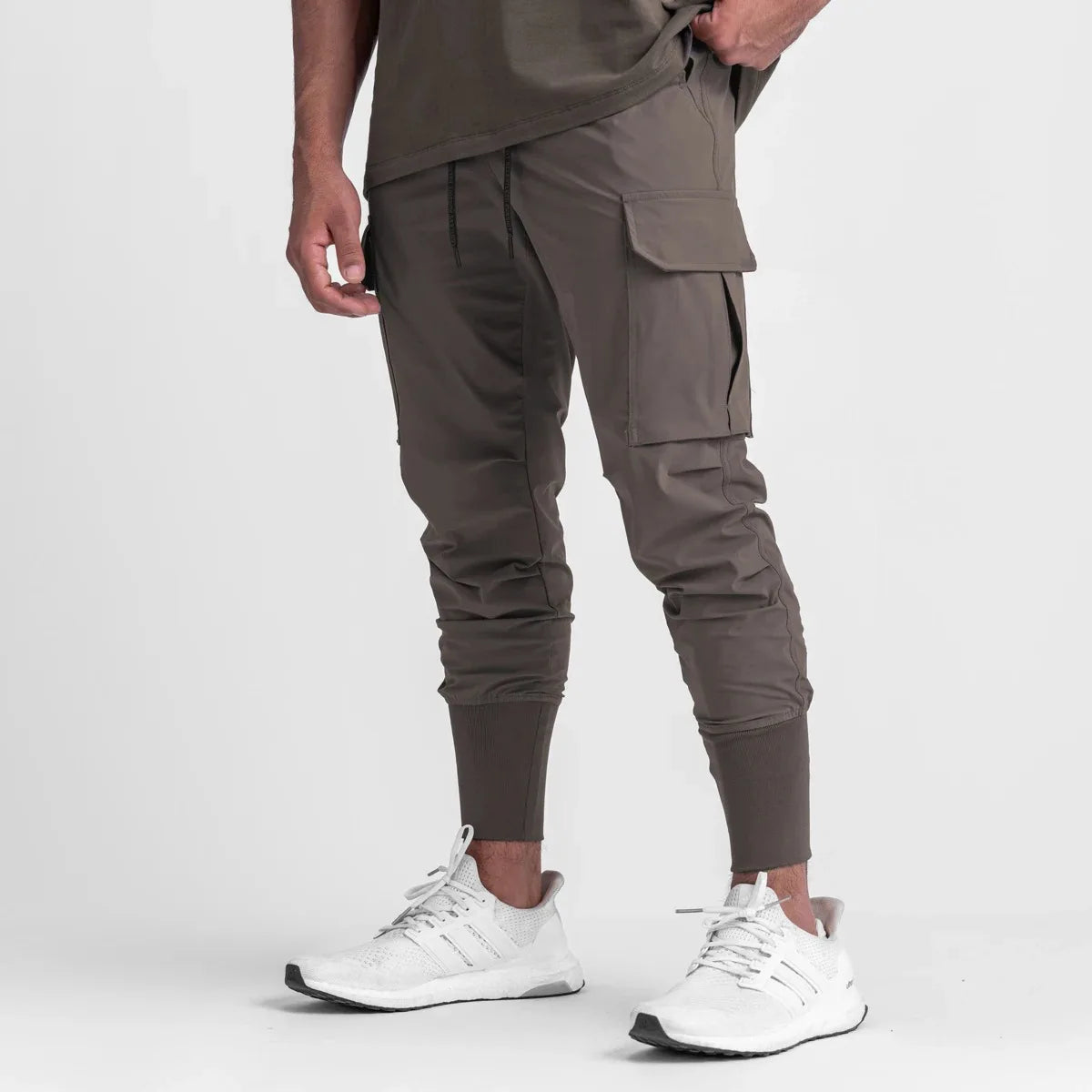 Men's cargo style sports pants in brown, featuring elastic cuffs and pockets, paired with white athletic shoes.