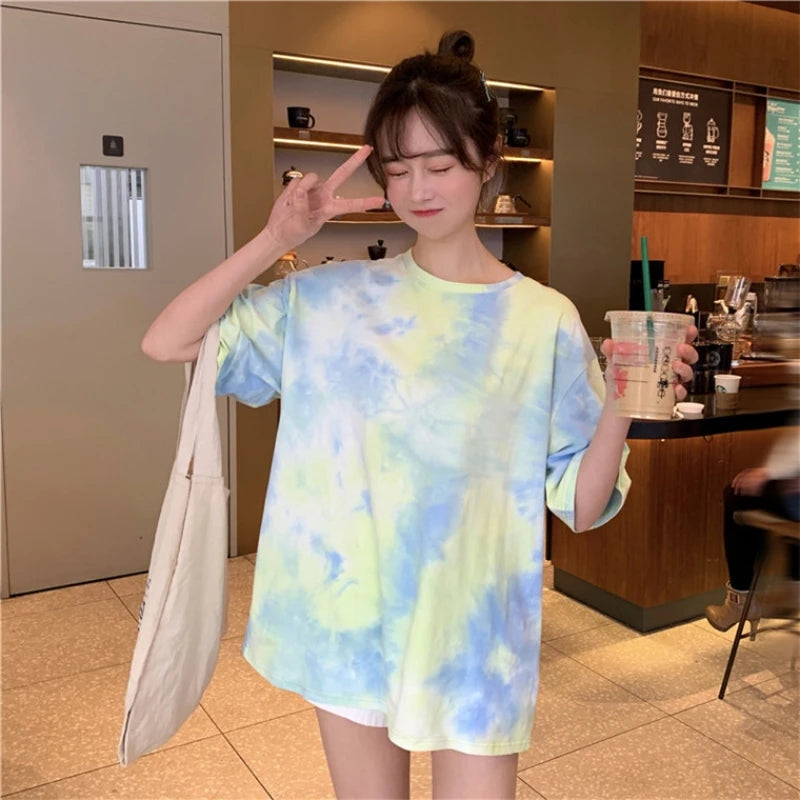 Model wearing a colorful tie-dye t-shirt in a cafe, showcasing a relaxed fit and vibrant pastel colors.
