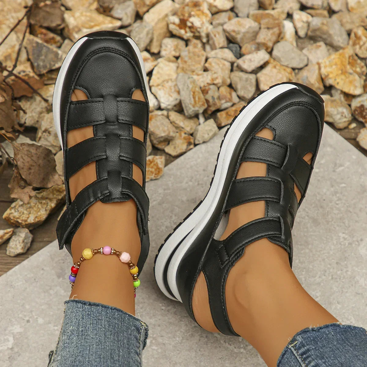 Black sandals with white soles worn on feet against a stone background