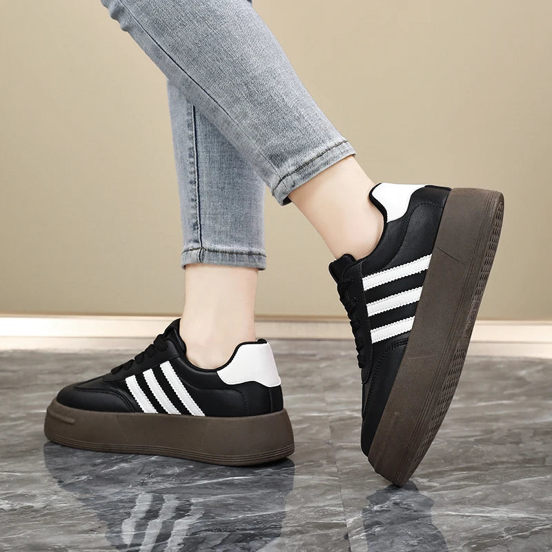 Black sneakers with white stripes worn on a wooden floor.