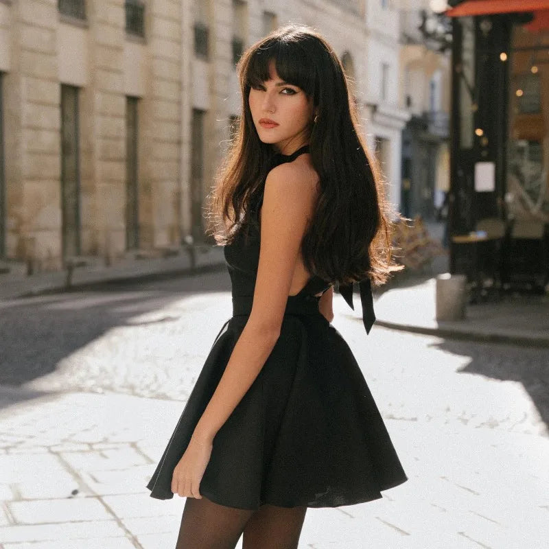 Model wearing a chic black halter dress in a city setting with a stylish A-line skirt and flowing hair.