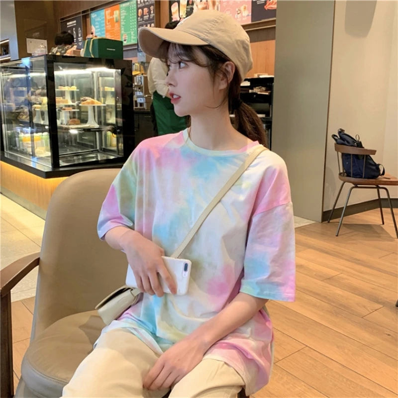 Young woman wearing a colorful tie dye t-shirt and a beige cap, sitting in a cafe.