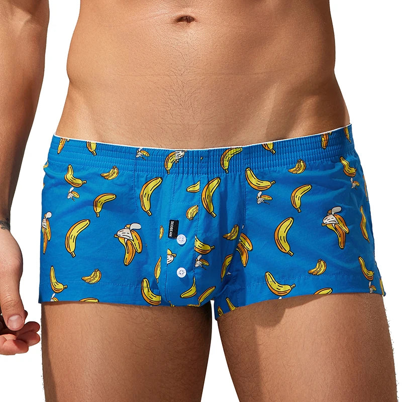 Men's boxer briefs featuring a bright blue base with a playful all-over print of bananas and cartoon characters, modeled on a person's lower torso against a plain white background.