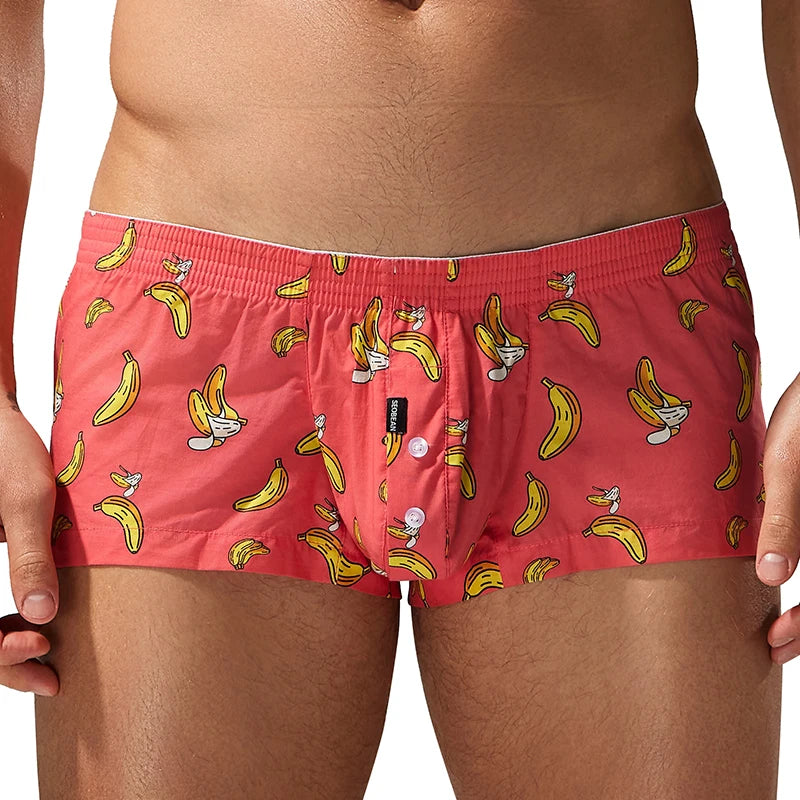 A close-up of a model wearing red boxer briefs with a yellow banana and cartoon character print, shown against a plain white background.
